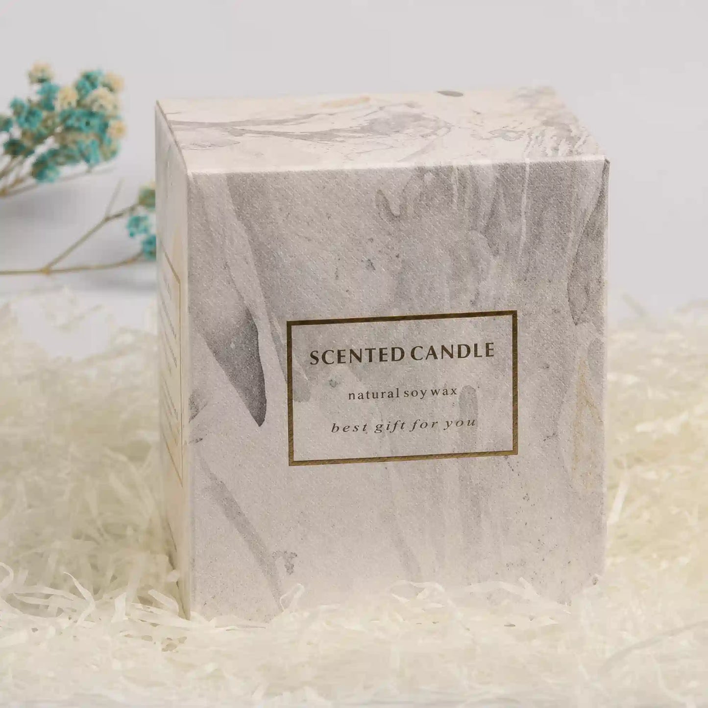 A square white and gray marble-patterned box for a scented candle, placed on white shredded paper. The front has a gold-bordered label reading 'SCENTED CANDLE' with smaller text 'natural soy wax' and 'best gift for you'.