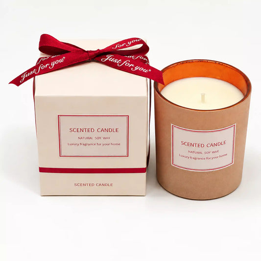 A scented candle in a metallic rose-gold container next to its cream-colored packaging box tied with a red ribbon that reads 'Just for you'.