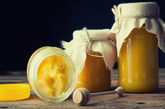 Jars of golden honey with crystallized honey and a honey dipper on a dark background.