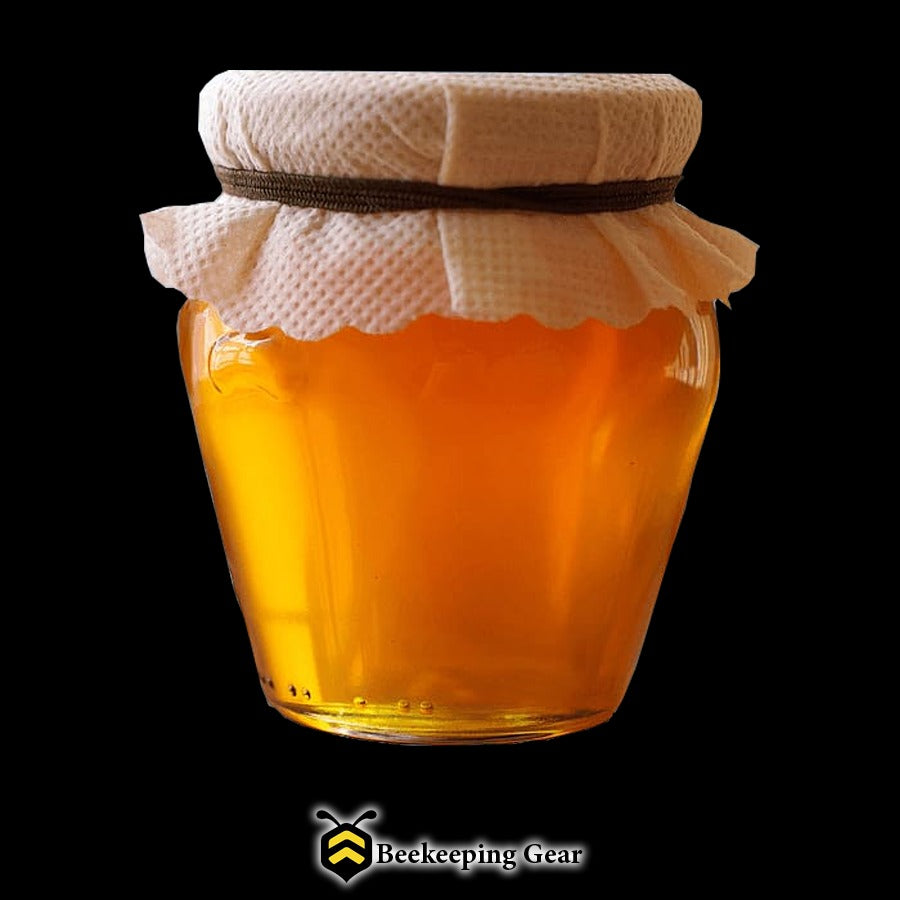 Glass jar of golden honey with a cloth cover on a black background.