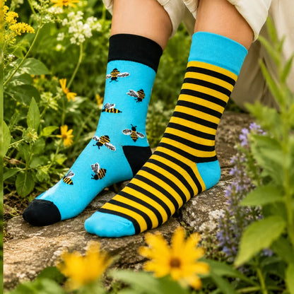 Person wearing bee socks in a garden, blue bee-print sock on one foot and yellow striped sock on the other