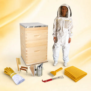 Beekeeper in a white suit beside a wooden beehive with a starter kit of smoker, hive tool, brush, gloves and wax foundation