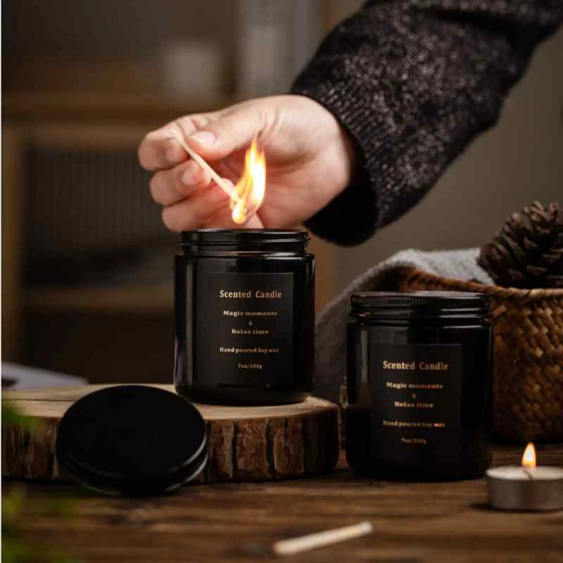 Black glass scented candle jars with lit match and cozy home decor scene.