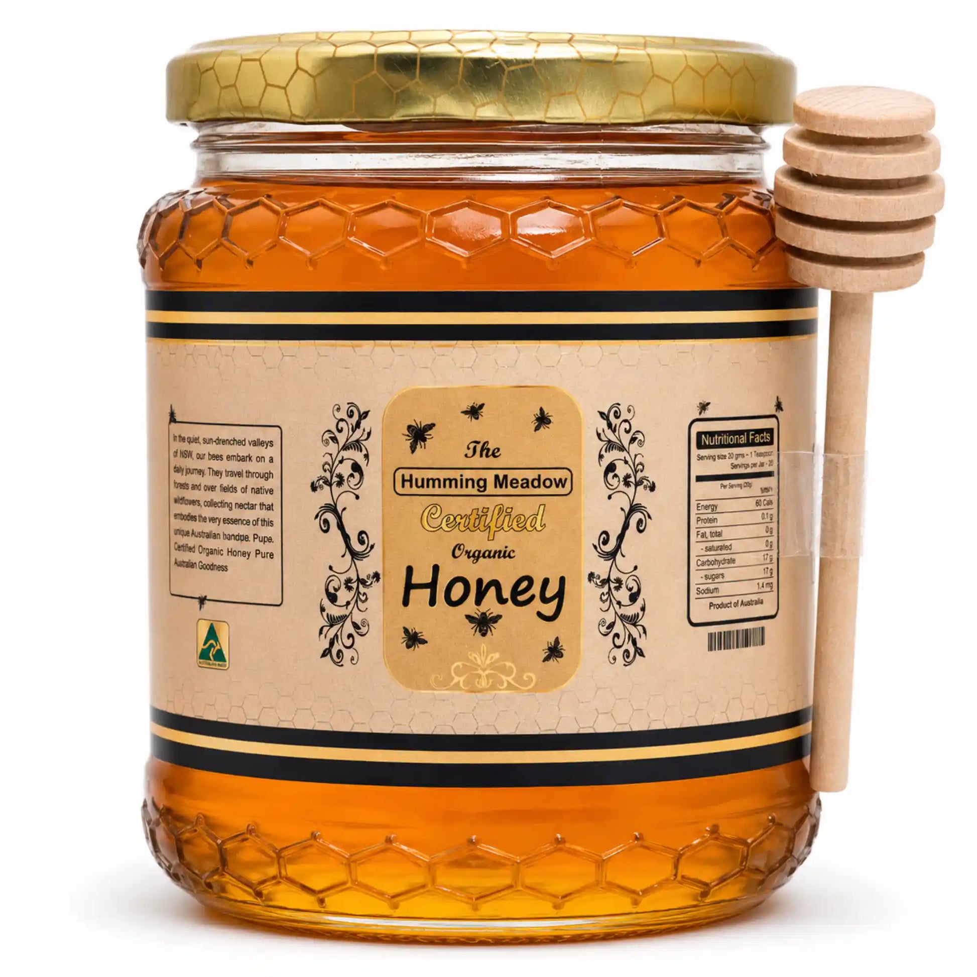 Glass jar of Humming Meadow organic honey with a gold honeycomb lid and a wooden honey dipper resting on top