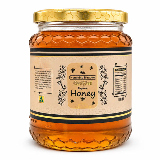 honey-glass-jar.webpGlass jar of Humming Meadow raw organic honey with honeycomb-textured base and gold lid on a white background