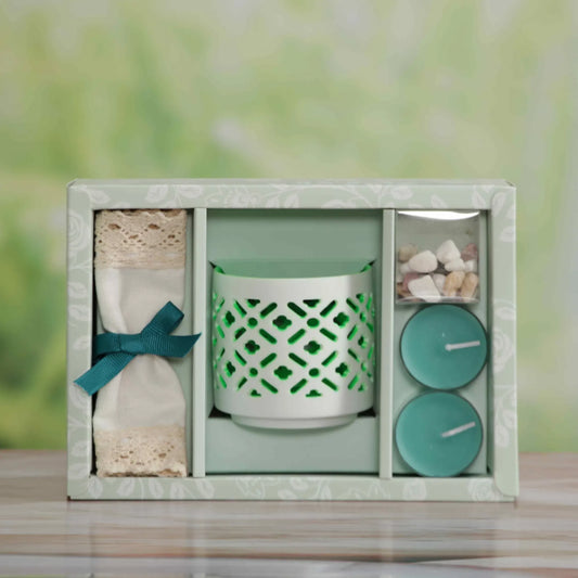 Jasmine Scented Candle, A gift set in a square box with a pale green floral pattern, containing a mint green patterned candle holder, a folded cream fabric item tied with a teal ribbon, and two round teal candles in a small clear container, set on a wooden surface with a blurred green background.