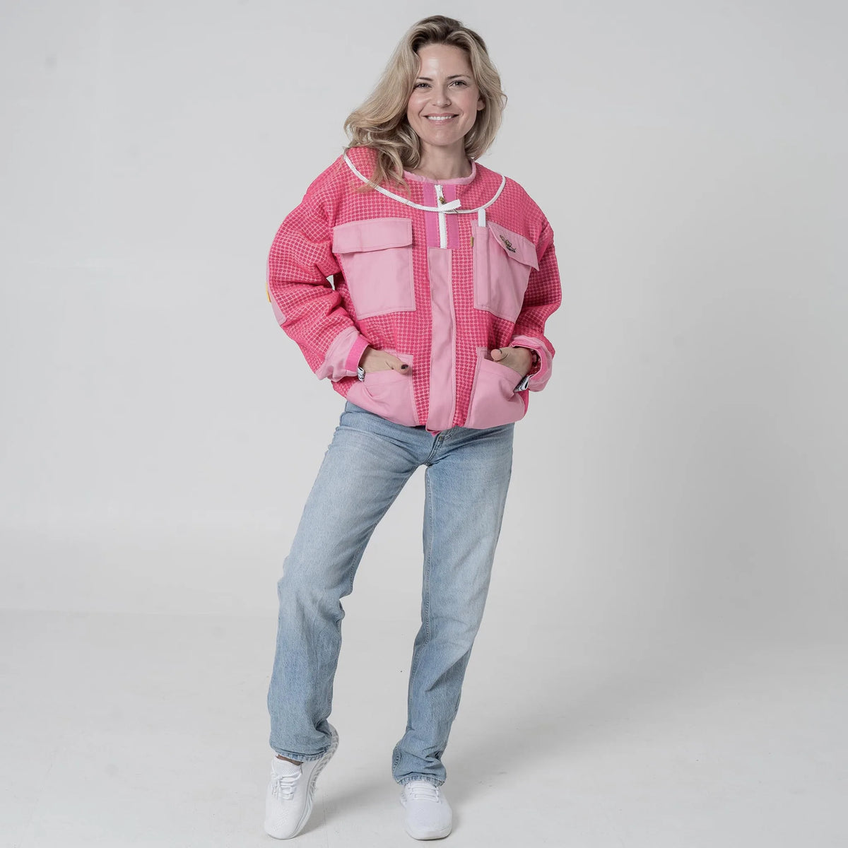 Woman wearing OZ Armour pink 3 layer mesh beekeeping jacket with hood removed, front view with hands in pockets