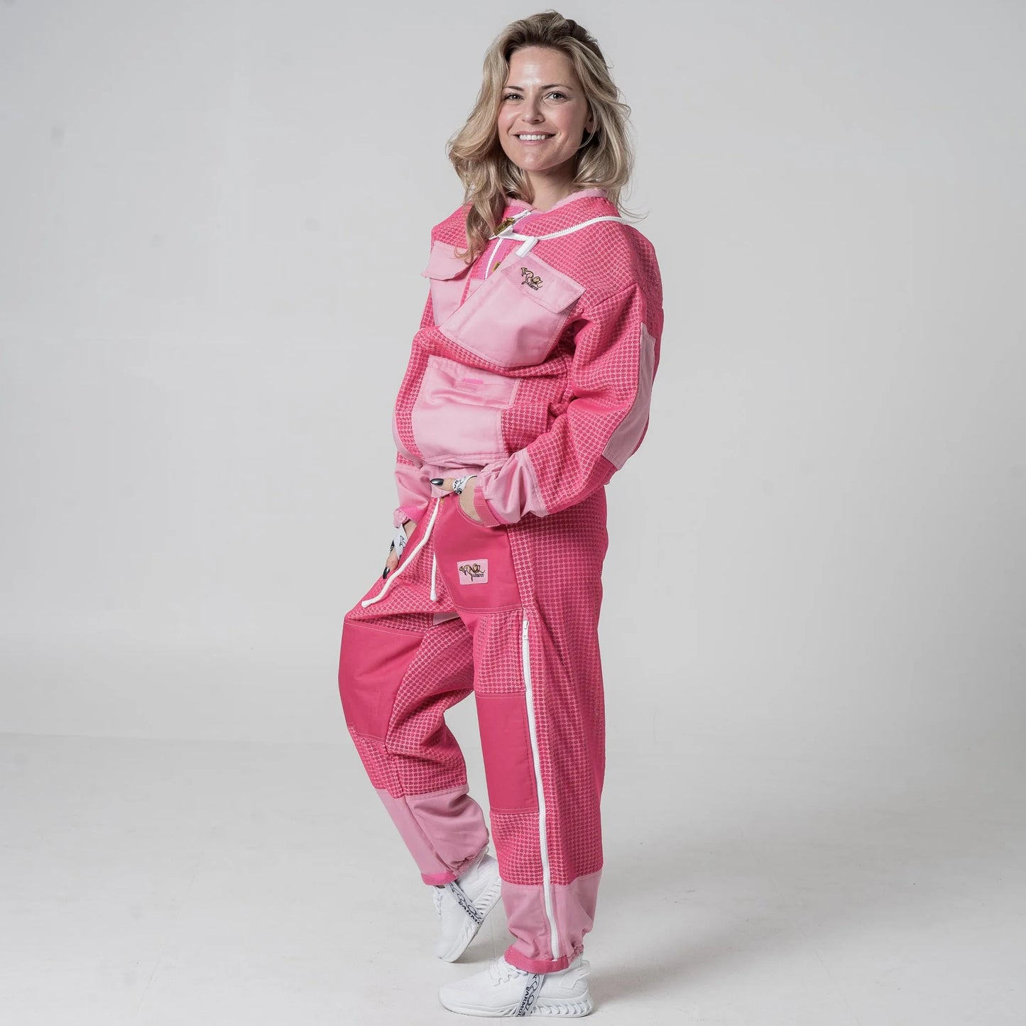 Woman wearing OZ Armour pink beekeeping jacket and trouser set with hood down, front view with hands in pockets
