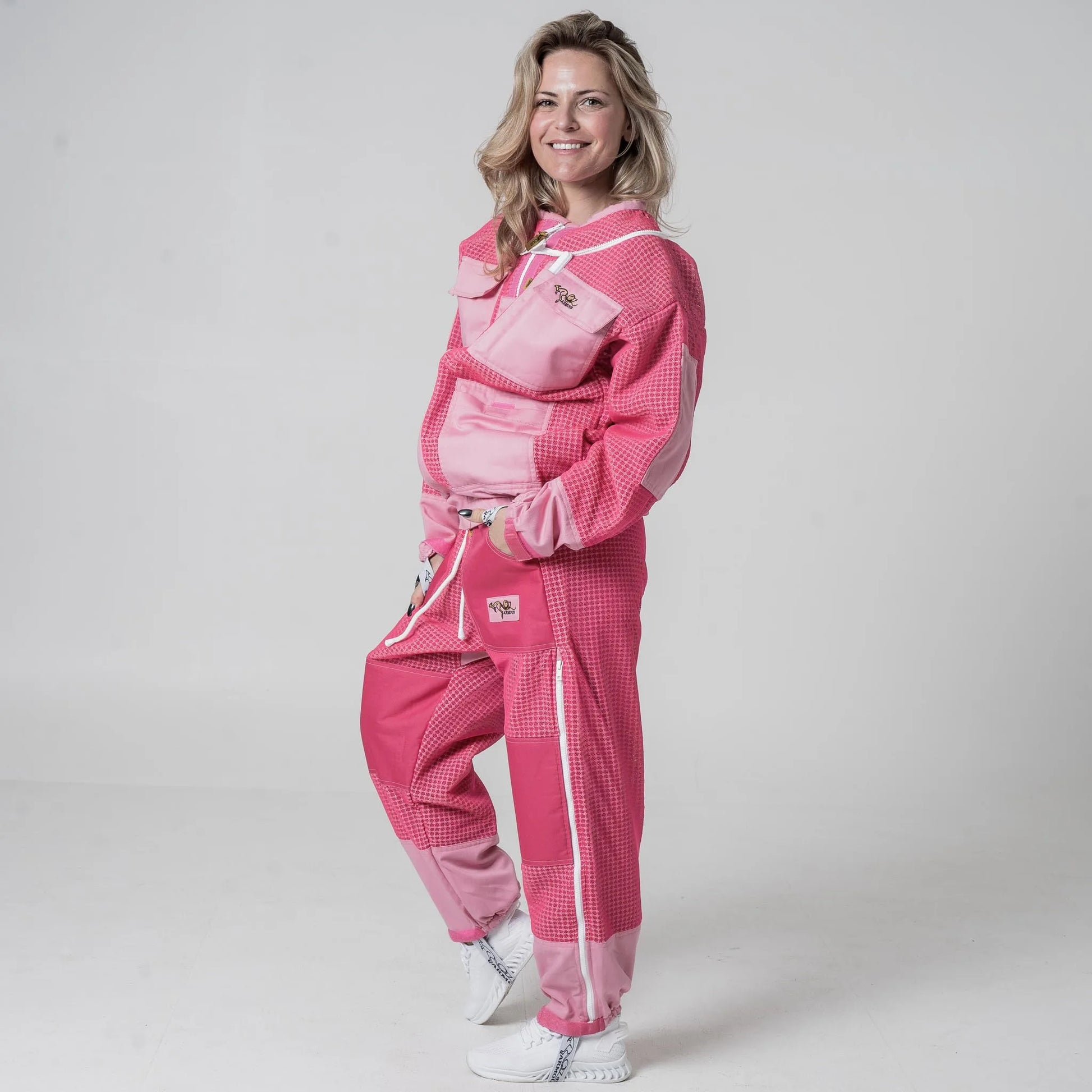 Woman wearing OZ Armour pink beekeeping jacket and trouser set with hood down, front view with hands in pockets
