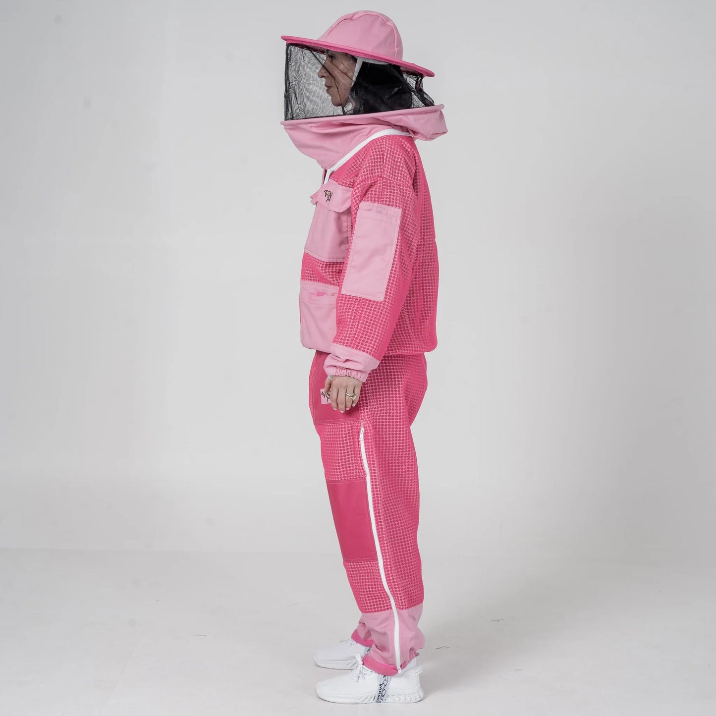 Woman wearing OZ Armour pink beekeeping jacket and trouser set with round hat veil hood up, side view
