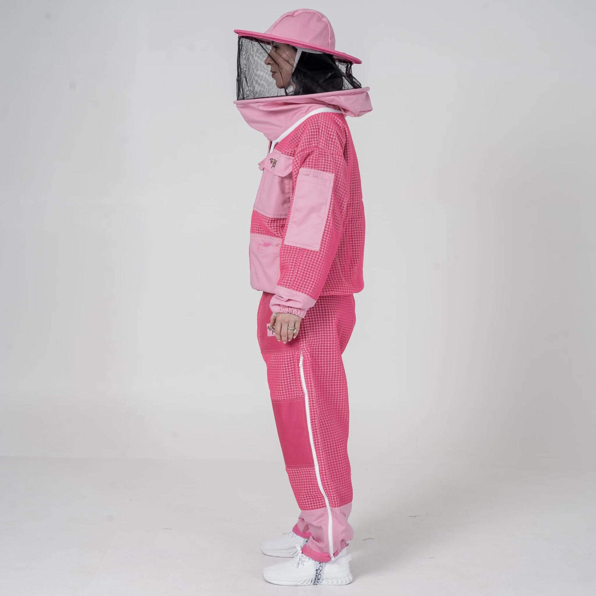 Woman wearing OZ Armour pink beekeeping jacket and trouser set with round hat veil hood up, side view
