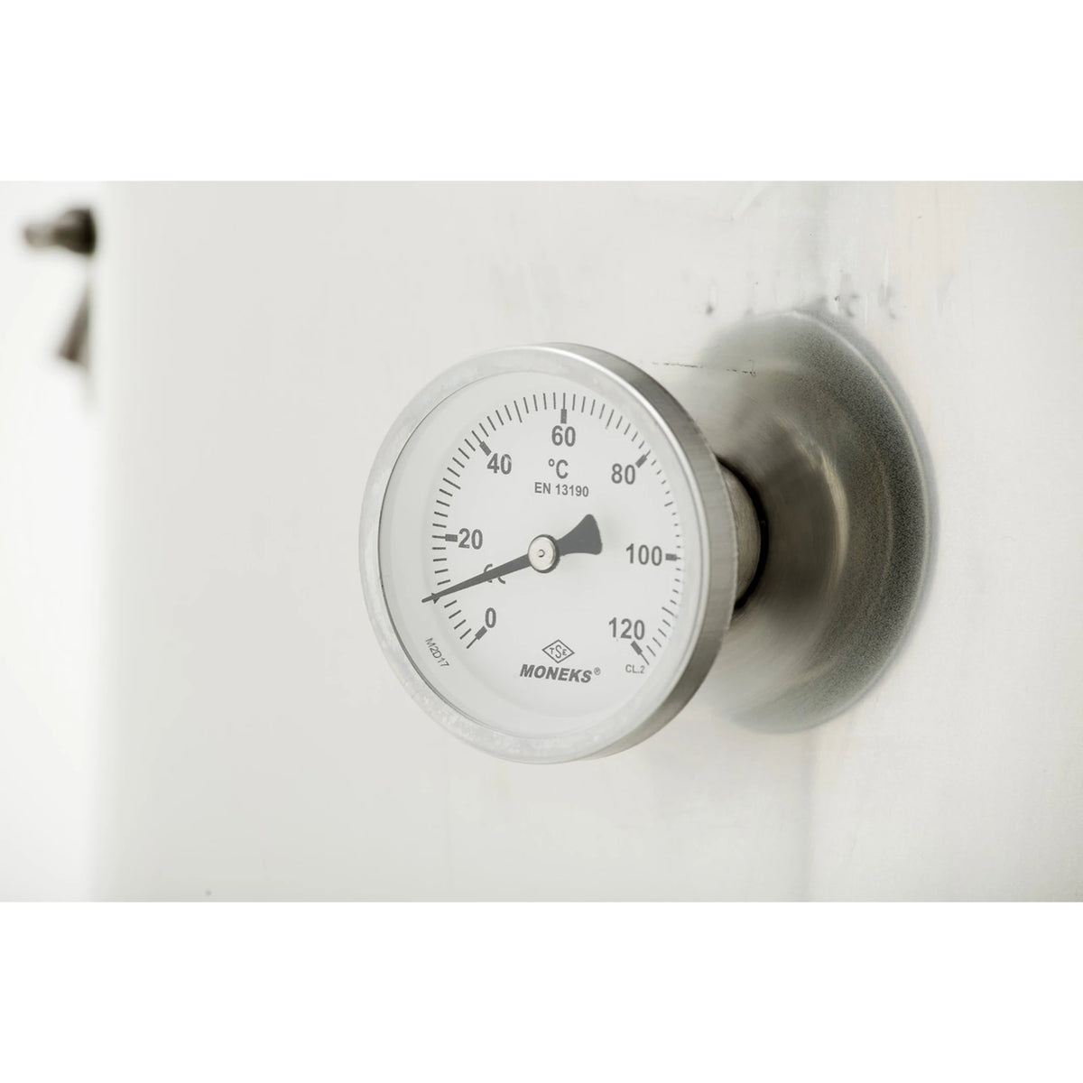 A Moneks temperature gauge with a silver metallic housing and a white dial showing temperature in degrees Celsius, mounted on a white surface.