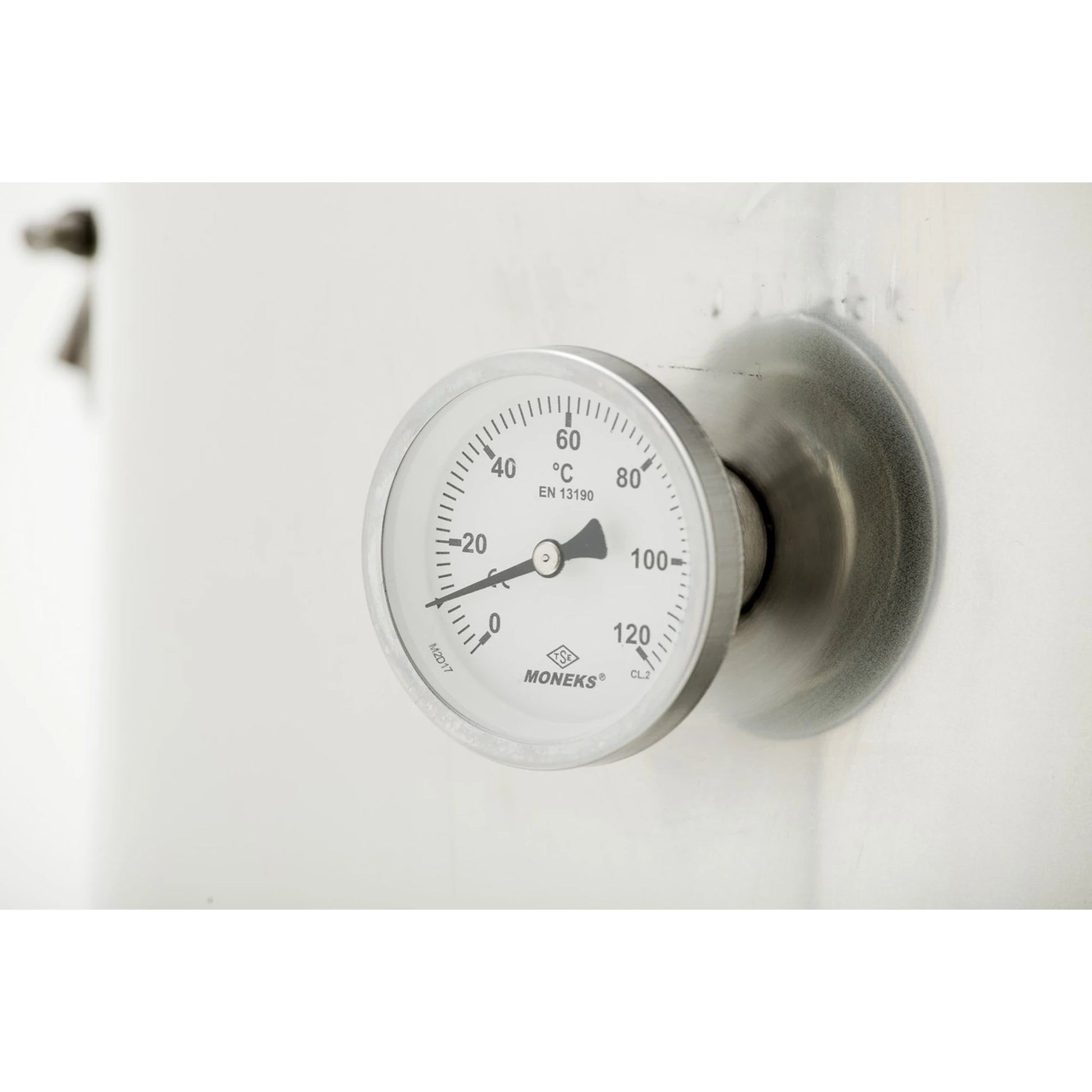 A Moneks temperature gauge with a silver metallic housing and a white dial showing temperature in degrees Celsius, mounted on a white surface.