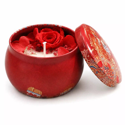 A red ceramic candle jar with a matching lid, featuring a red rose and red flower petals on the wax inside, set against a plain white background.
