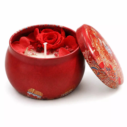 A red ceramic candle jar with a matching lid, featuring a red rose and red flower petals on the wax inside, set against a plain white background.