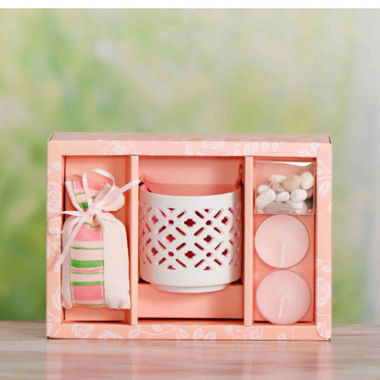 A rose scented candle in a pink box with a clear lid, displaying the candle, a candlestick, and decorative pebbles.
