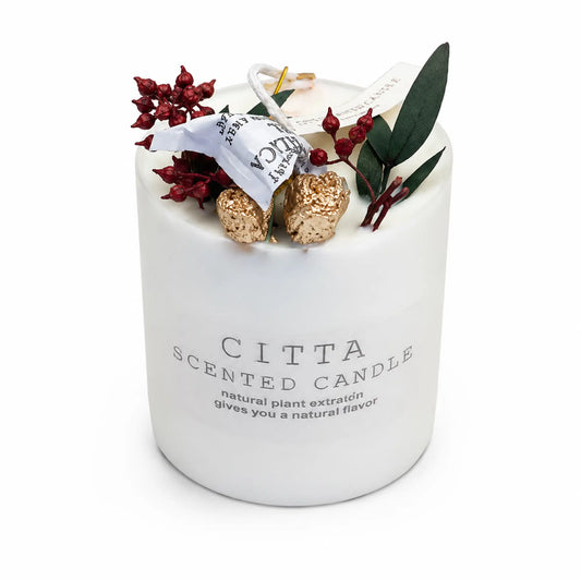 A white scented candle jar labeled 'CITTA SCENTED CANDLE' with decorative dried red berries, green leaves, and gold glitter accents on top, photographed on a clean white background.