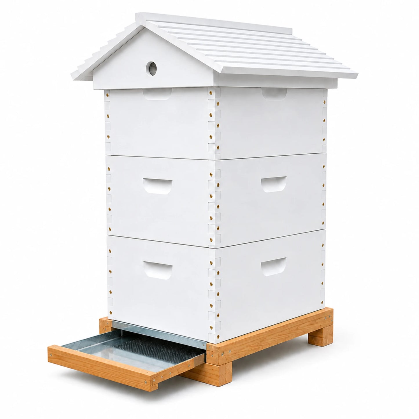 Angled view of a white wooden beehive with a cottage-style roof, three stacked boxes, and a galvanized slide-out debris tray on a natural wood base